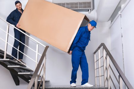 Professional workers carrying refrigerator on stairs indoors